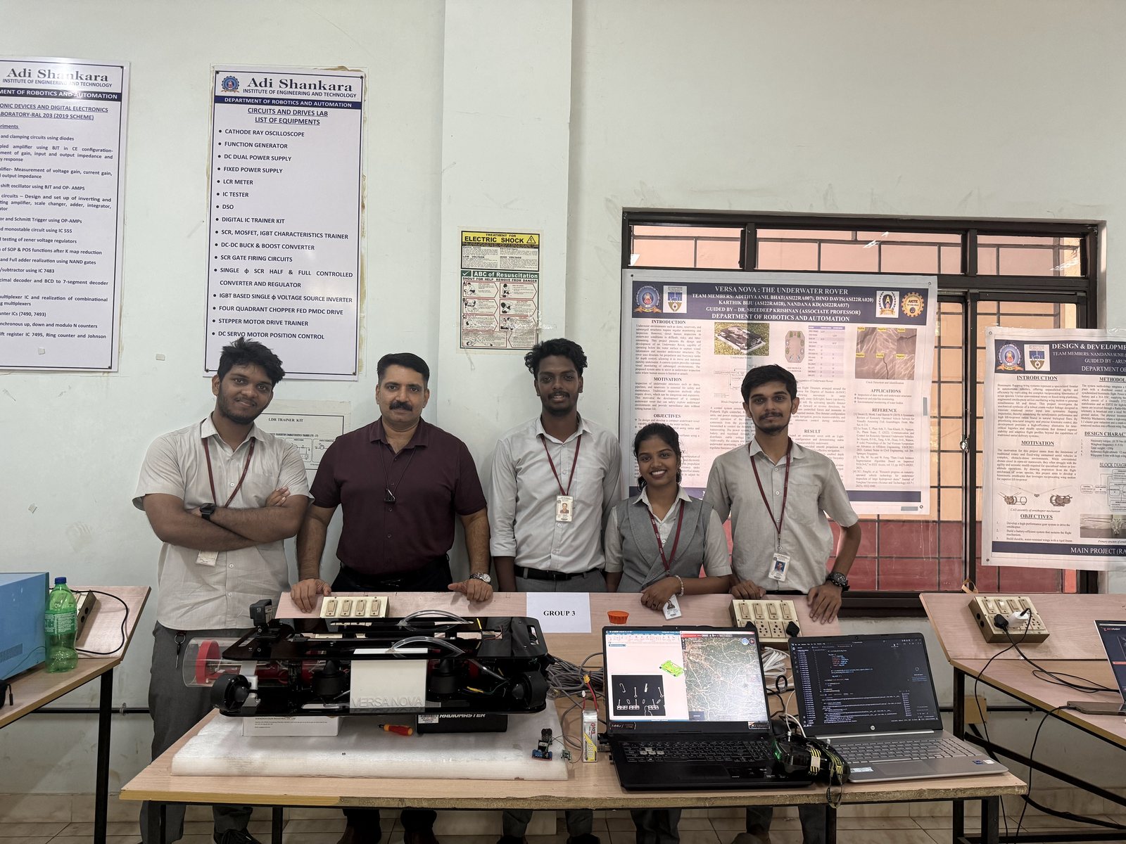 The Versa Nova team and their guide standing behind the rover, with the project poster on the wall